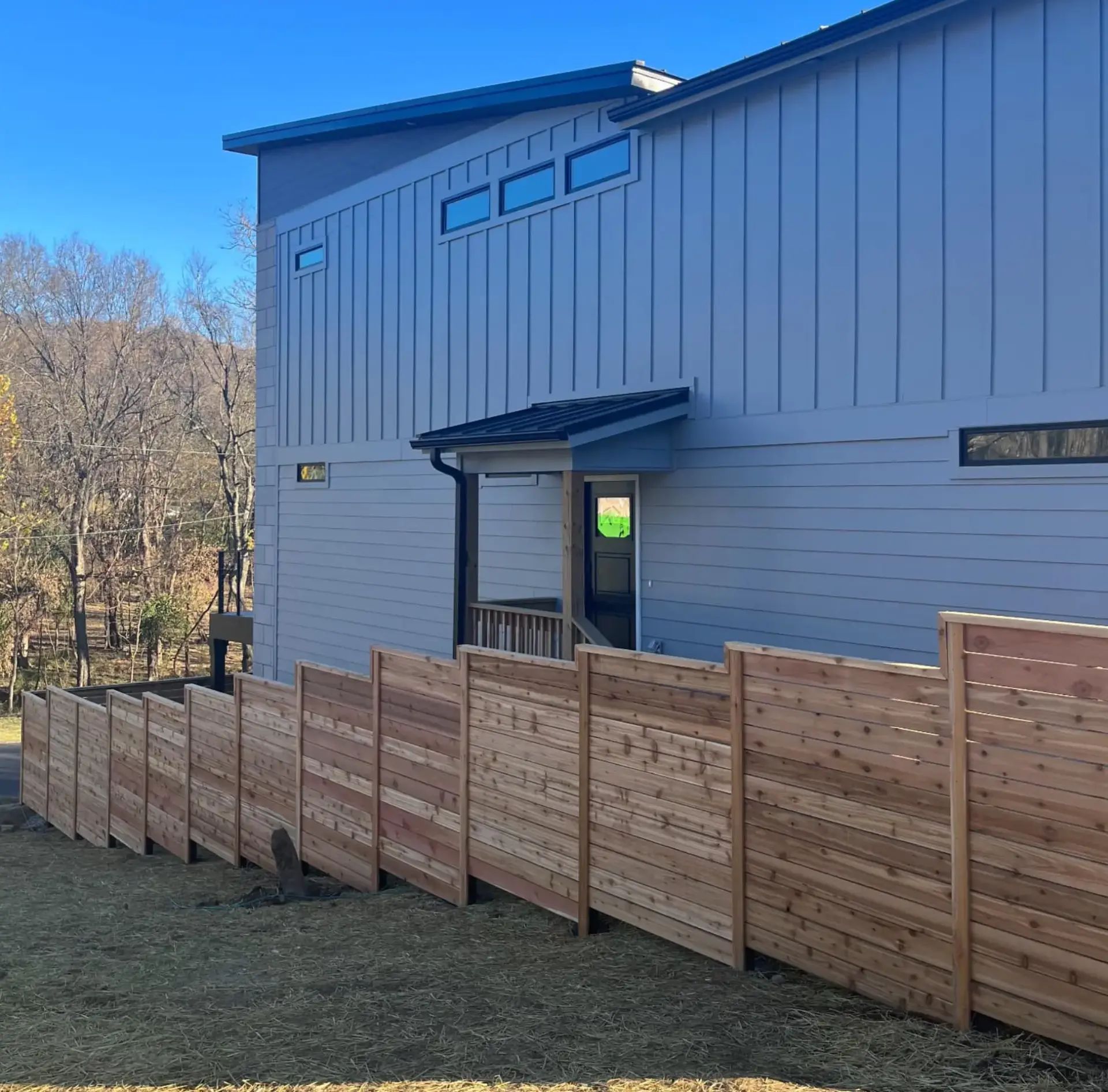 Luxury horizontal cedar picket fence around a modern multistory home, featuring black metal posts and black steel gate frames.